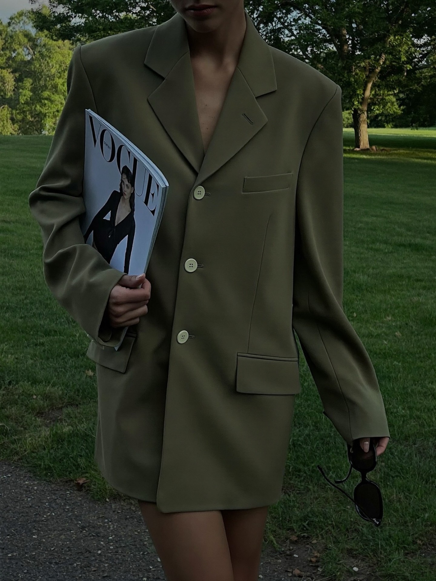 A fashion editorial portrait featuring an oversized green blazer and magazine.