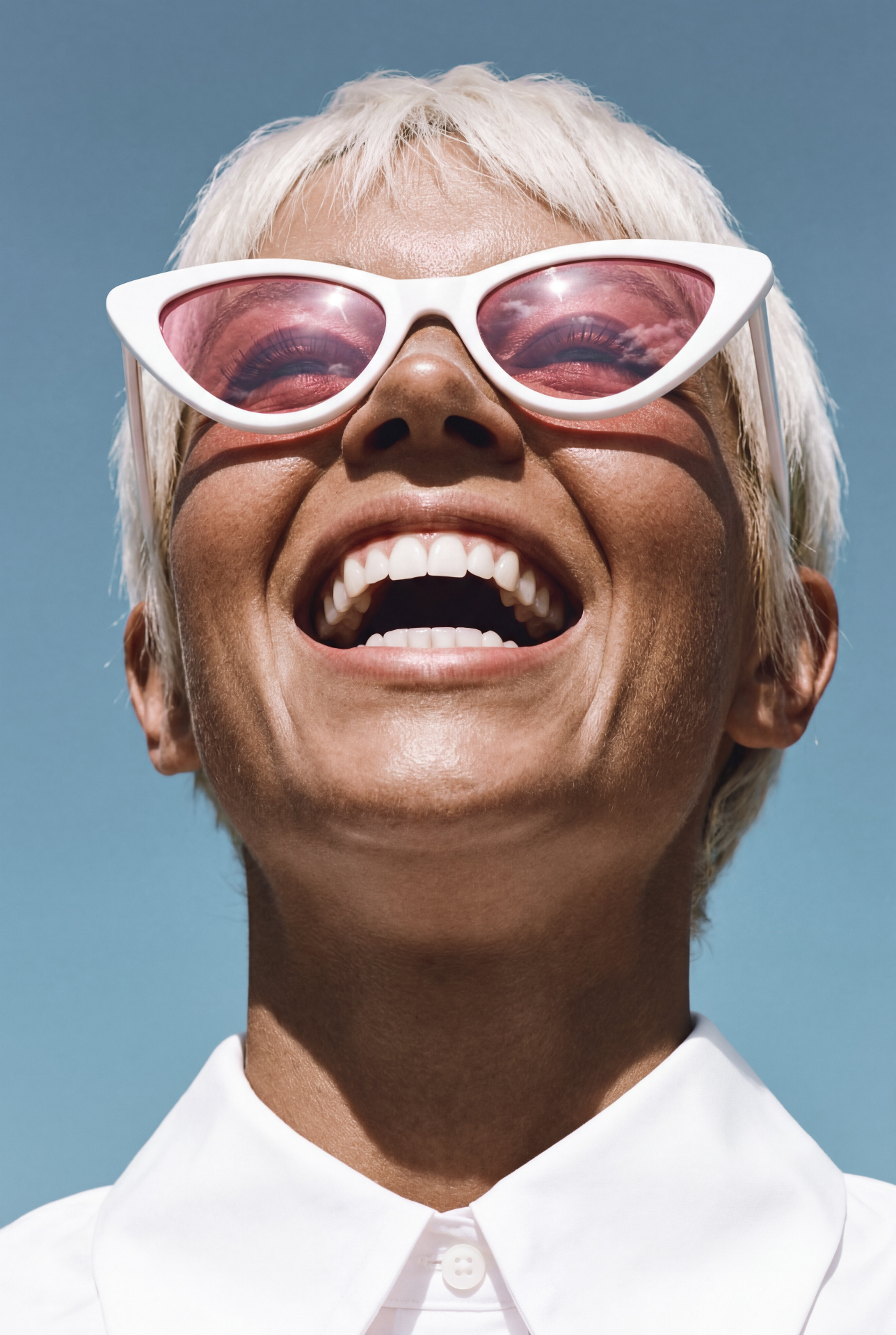 A smiling person in white cat-eye sunglasses against a blue sky.